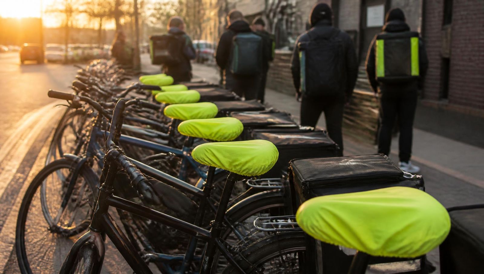 A row of delivery bikes with matching branded neon seat covers at golden hour