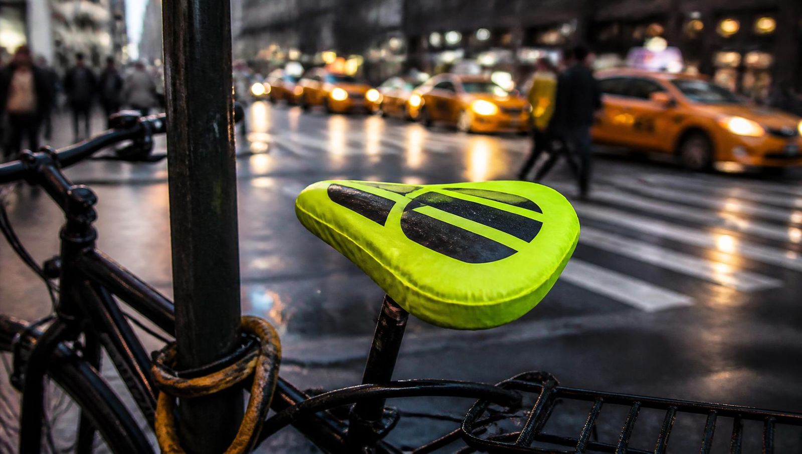 Bicycle parked on a wet New York street at dusk with a branded neon-yellow seat cover in the foreground