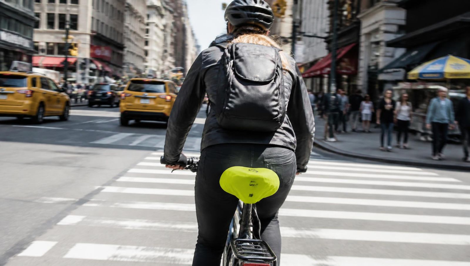 Cyclist riding through a busy New York intersection with a branded seat cover