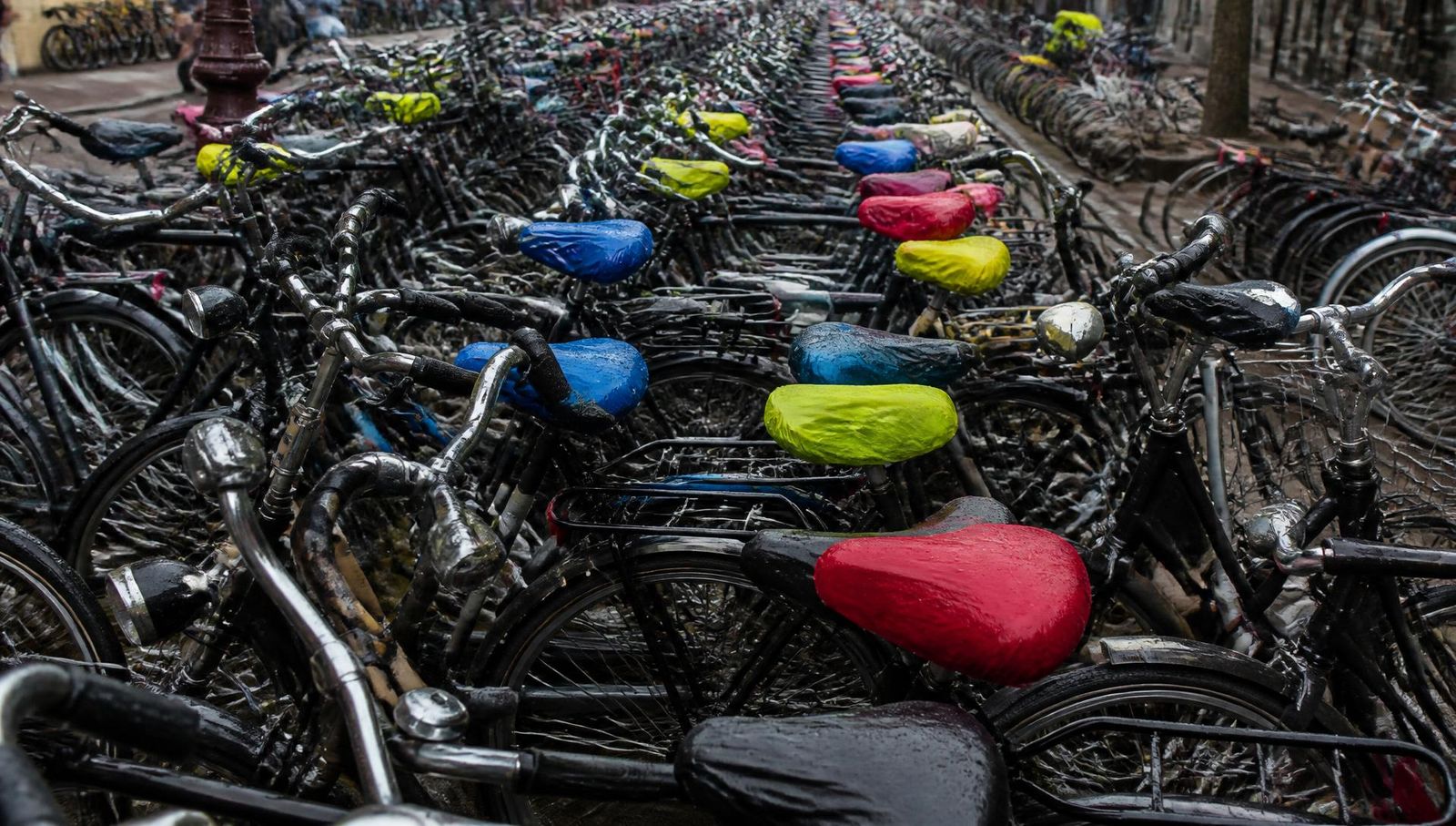 Dozens of parked bikes with colored seat covers filling a bike rack